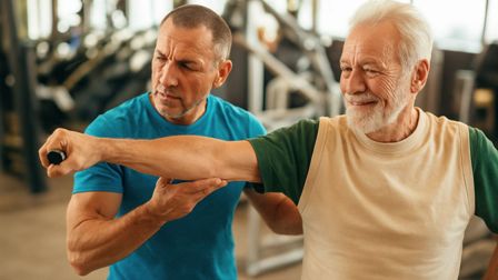 Image of a senior-aged personal trainer coaching an older adult male.
